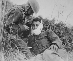 A wounded soldier of Company K, 110th Infantry, receiving first-aid treatment from a comrade at Varennes-en-Argonne, France, September 26, 1918. National Archives