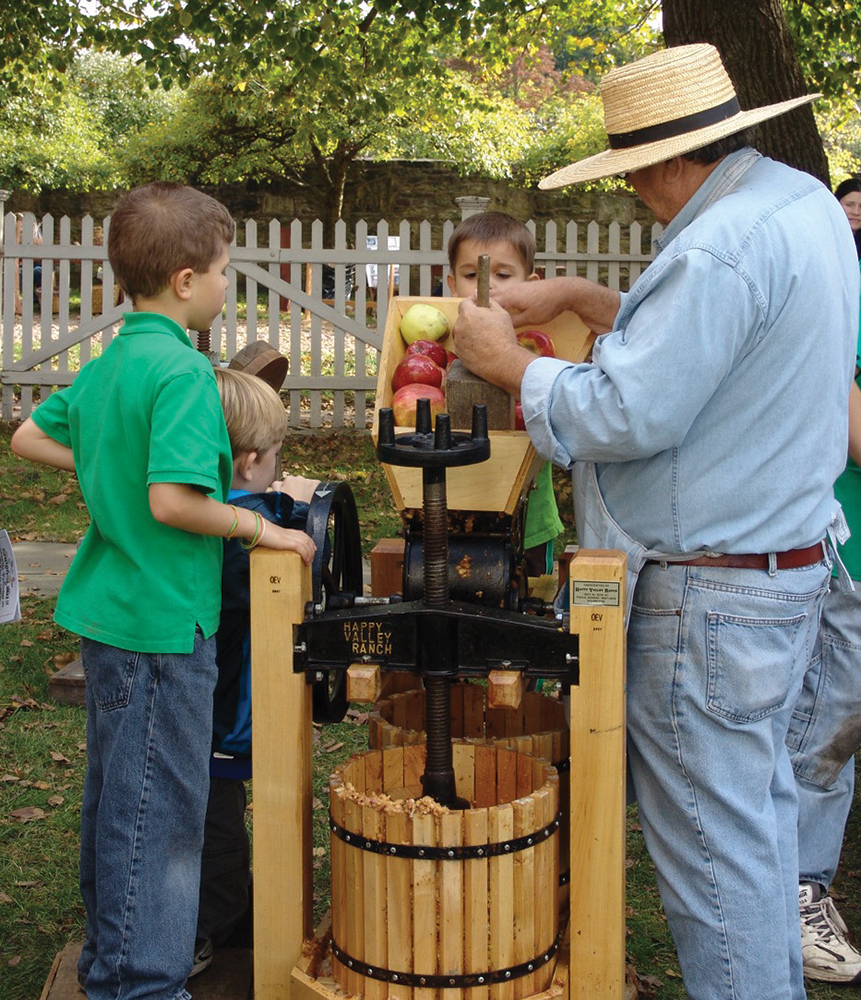 Volunteer Jack Holbrook demonstrates a 19th century-style cider press for young attendees at Erntedankfest.