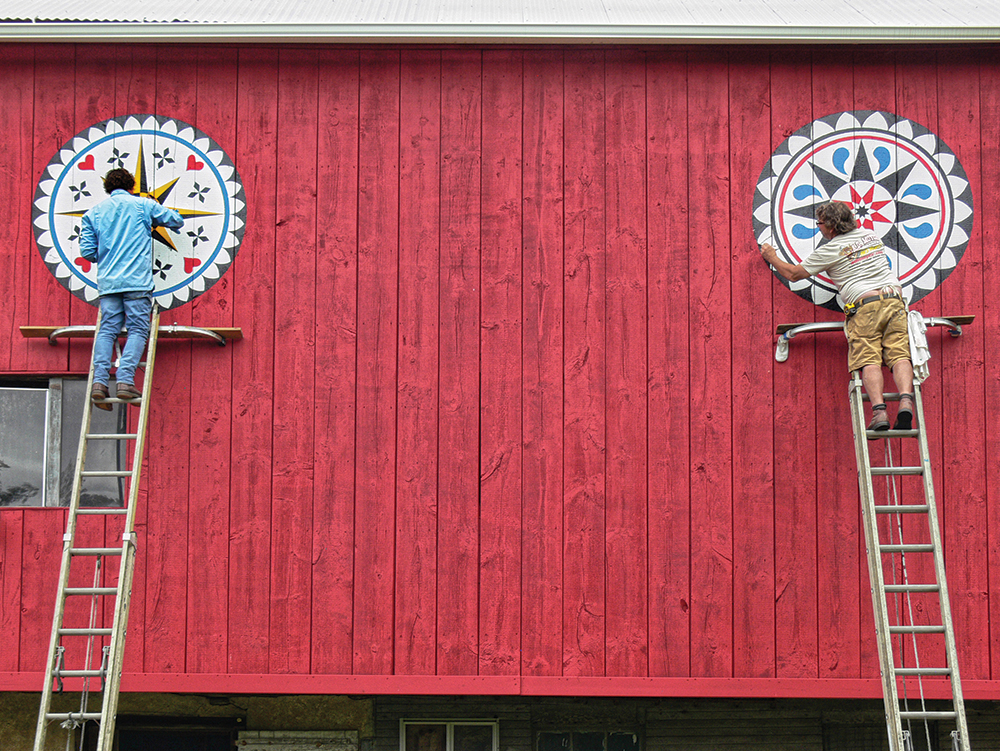 Two barn star painters, Eric Claypoole and Andrew Shirk, work on the Hutchinson Barn, near Vera Cruz, in 2020. The barn features star patterns, distinctive to the Lehigh Valley region, with raindrops and floral borders. Photo, Patrick J. Donmoyer