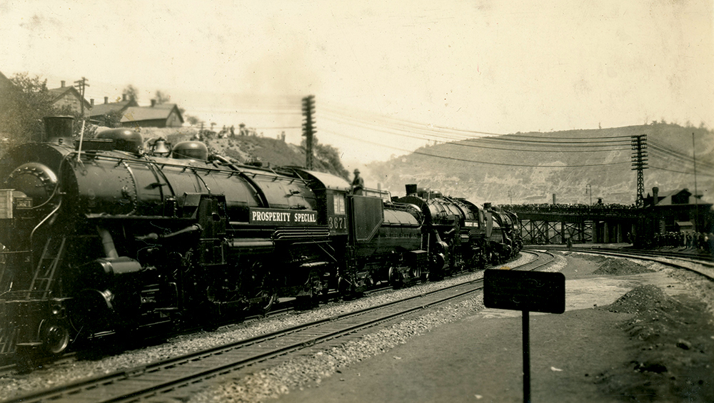 A crowd on a distant overhead bridge admires the Baldwin “Prosperity Special” as it moves through Johnstown, Cambria County, in May 1922. The headlights, as seen at far left on the nearest engine, were boxed with wooden covers to prevent breakage or vandalism during the long cross-continent journey to California. Collection of Dan Cupper