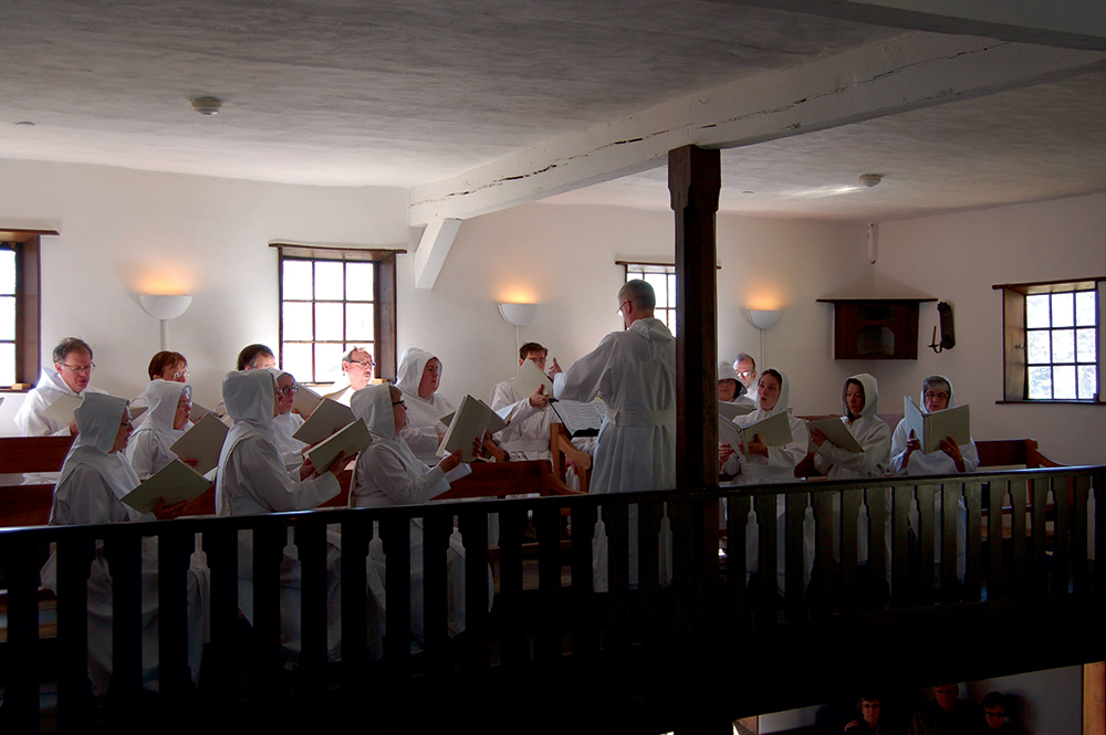 The lyrics and melodies of the music created at Ephrata can still be heard in concerts and recordings by the Ephrata Cloister Chorus. Here the chorus performs from a balcony in the Saal. Ephrata Cloister, PHMC