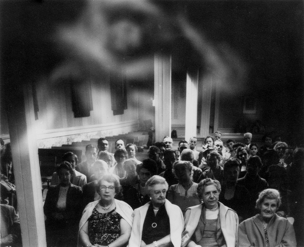 At Camp Silver Belle, visitors posed for photographs that when printed revealed spirits in close proximity to the sitters. In this mid-20th-century spirit photograph, several camp visitors sit in an auditorium as a ghostly ectoplasm circles above. Collection of Alan E. Mays