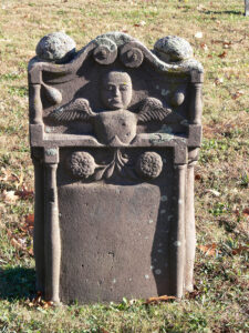 An elaborate winged angel head peers out from the pediment of this red sandstone gravemarker at Muddy Creek Lutheran Church in Denver. This undated example is among the many “blank” gravestones that once featured painted inscriptions at this cemetery. Photo, Patrick J. Donmoyer