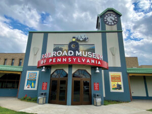The new front entrance signage at the Railroad Museum of Pennsylvania, installed in March 2024, showcases a silhouette of Pennsylvania Railroad steam locomotive No. 1223, along with the working 8-foot Seth Thomas Clock, adorning the clock tower since 2007. Railroad Museum of Pennsylvania, PHMC